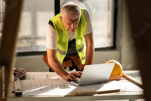 Construction Worker Uses Laptop at Construction Site to Check Plans and Manage Tasks During Working Hours in Bright Daylight