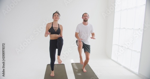 Tableau sur toile A fit couple performs a synchronized high-knee cardio exercise on yoga mats in a bright white studio, focusing on core strength and physical wellbeing together