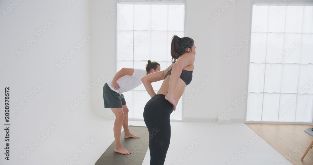 Fototapeta premium A fit couple performs a synchronized warm-up stretch together in a bright, minimalist yoga studio, focusing on flexibility and wellbeing before their workout.