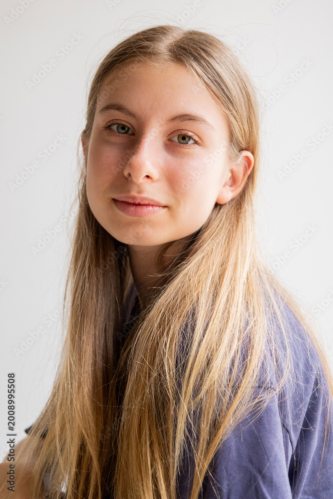 Fototapeta premium Portrait of a 12-year-old blonde pre-teen girl wearing a blue sports t-shirt and blue jeans against a white background