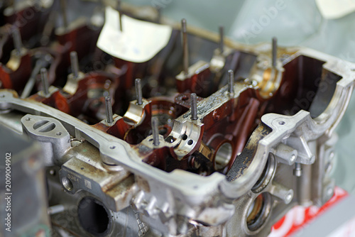 A partially disassembled engine cylinder head shows camshaft bearing seats, studs, and oil channels, with visible oil residue indicating ongoing inspection or repair work.