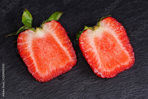 Fotografie Halved fresh garden strawberry with sepal on black slate plate