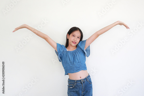 Cheerful young girl in stylish blue denim crop top and jeans posing with her arms wide open against white background.