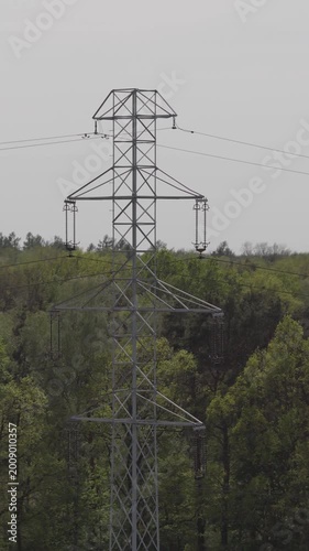 Drone footage of high-voltage traction lines humming under a brilliant sunny sky, framed by lush forest 