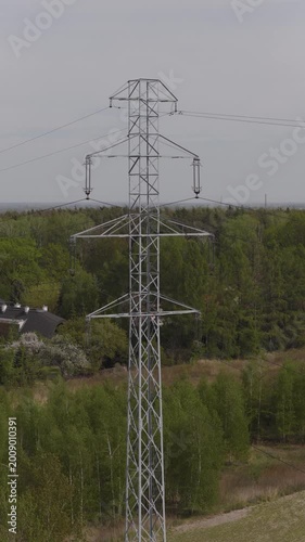 Drone footage of high-voltage traction lines humming under a brilliant sunny sky, framed by lush forest 