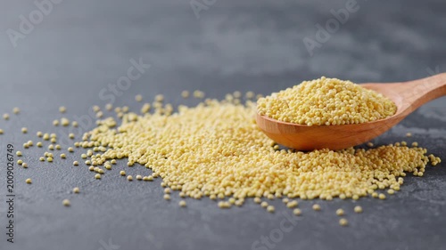 organic millet in a wooden spoon on a dark kitchen table. millet grains in a wooden spoon on a black marble background.