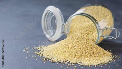 millet grains out of a glass storage jar on a dark kitchen table. organic millet spill out of a glass storage jar a black marble background.