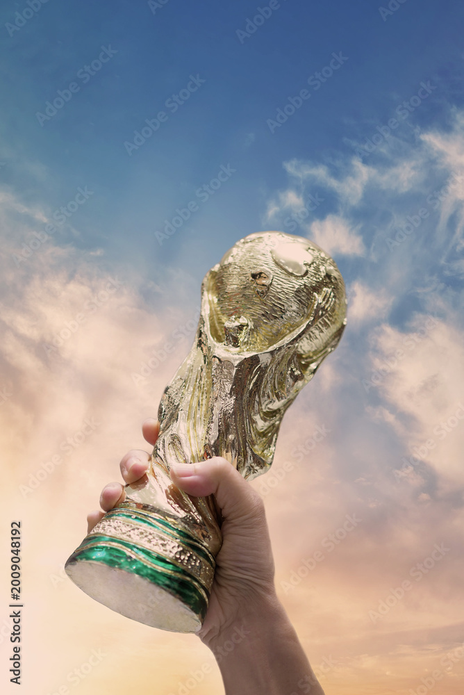 Fototapeta premium Bangkok Thailand. May 4 2026. Mock Up of the FIFA World Cup Trophy in hand and sky Background. Man holding a trophy of the FIFA World Cup in hand. Fifa 2026 winning trophy is raised up in the air.