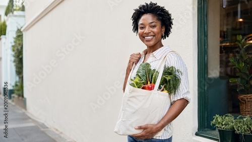 African American woman smiling while carrying a tote bag of vegetables  