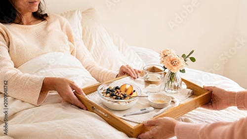 Woman receiving breakfast in bed on tray with flowers and drink  