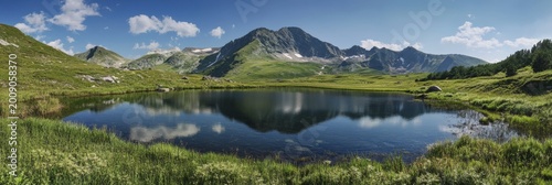 Mountain lake reflects sky and landscape during daytime with clear water and green grass nearby