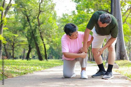 Senior woman having knee pain while jogging in the park with her husband. Osteoarthritis, joint inflammation, and health problems in elderly concept. copy space