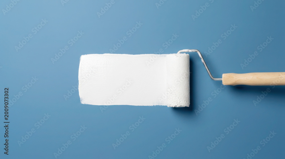 Obraz premium Paint roller with white paint on a blue background, showcasing a clean and modern design suitable for home improvement projects