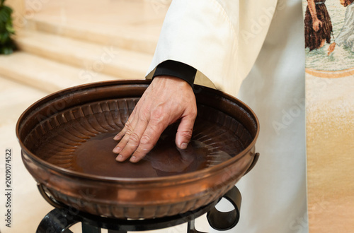 Priest's hand touching water in baptismal font