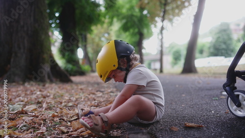 Obraz na płótnie Toddler sitting on park pathway wearing yellow helmet after minor fall, looking