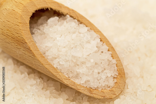 Tableau sur toile Close-up view of wooden scoop filled with sea salt on white salt background