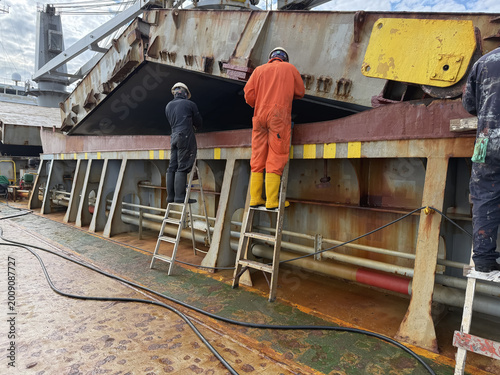 ship crew painting coaming of ship cargo holds. hatch covers opened by pyramid. team work. seafarers life.