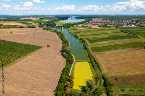 Fotografie Aerial view of fishpond system and agricultural fields near Hlohovec, South Moravia, Czech Republic on a sunny summer day with rural village in the background