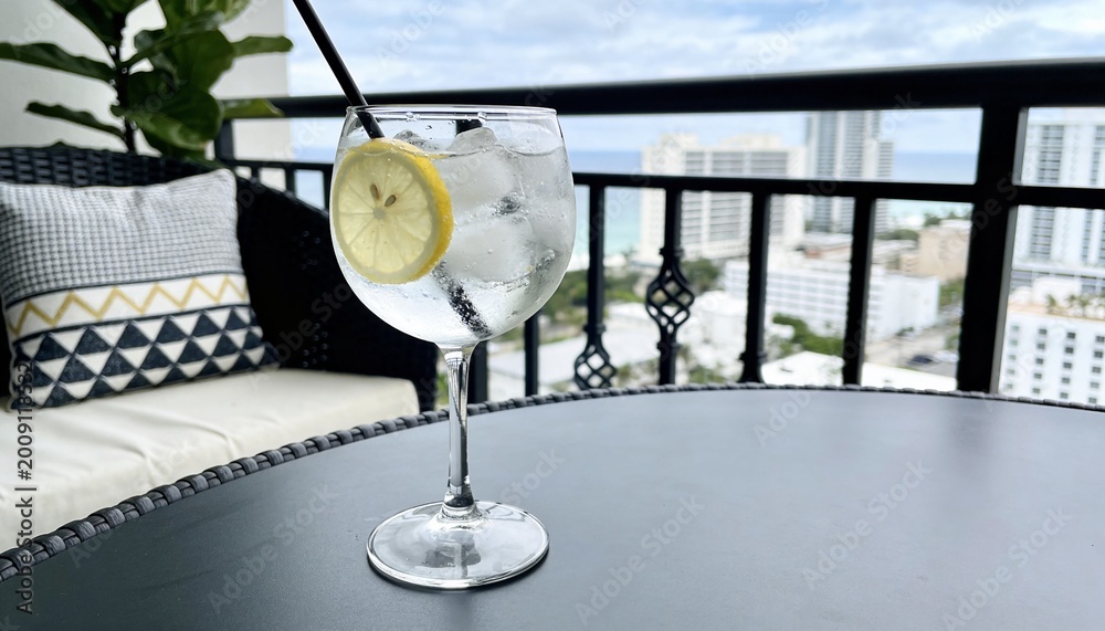Naklejka premium Refreshing gin and tonic cocktail with lemon and ice on a balcony.