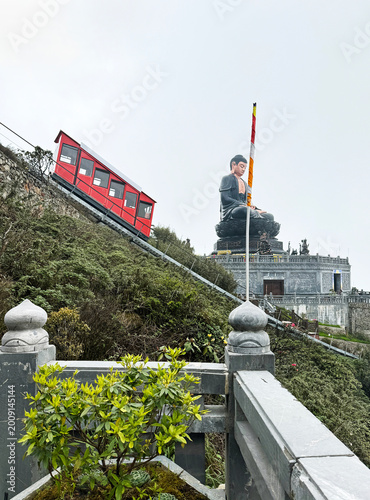 Photography Scene of a red furnicular train going down from peak with giant Buddha statue at the background