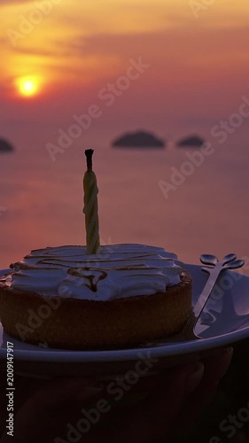 Vertical video. Close View of Birthday Cake with Candle on Plate against Blurred Ocean Sunset Background Warm Evening Light Celebration and Travel Lifestyle Scene