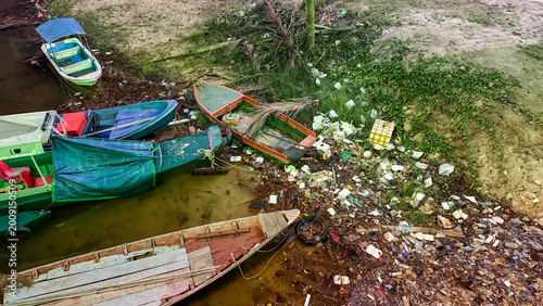фотографія Riverbank pollution with plastic waste near small boats highlighting environment