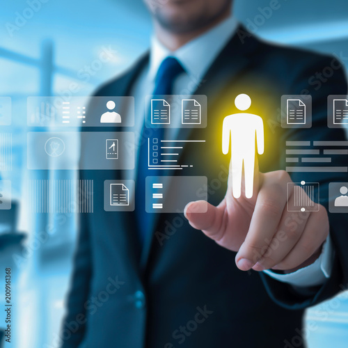 A professional business photo of a person in a dark suit and blue tie interacting with a holographic user interface.