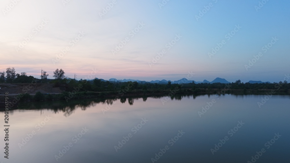 Naklejka premium Landscape sunset over chumphon river, still water reflecting sky and mountains