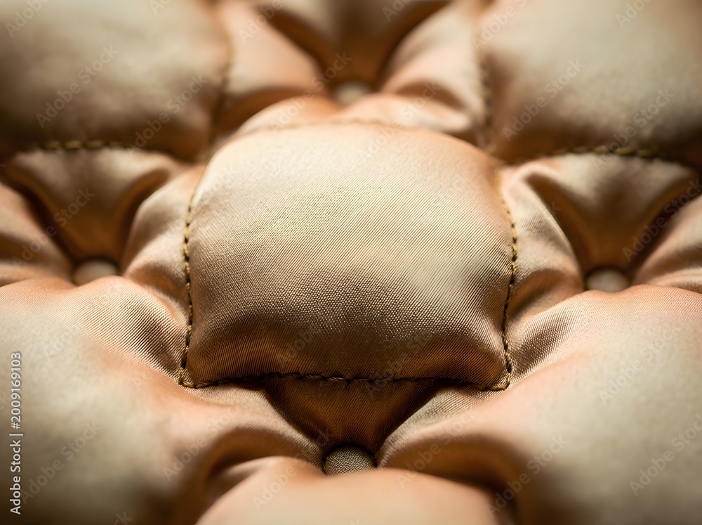 Fototapeta premium Close-up of luxurious champagne gold quilted satin fabric with deep tufted texture and soft iridescent sheen