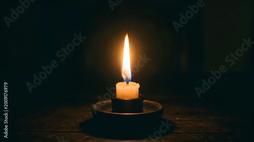 A single burning candle with a bright flame against a dark background