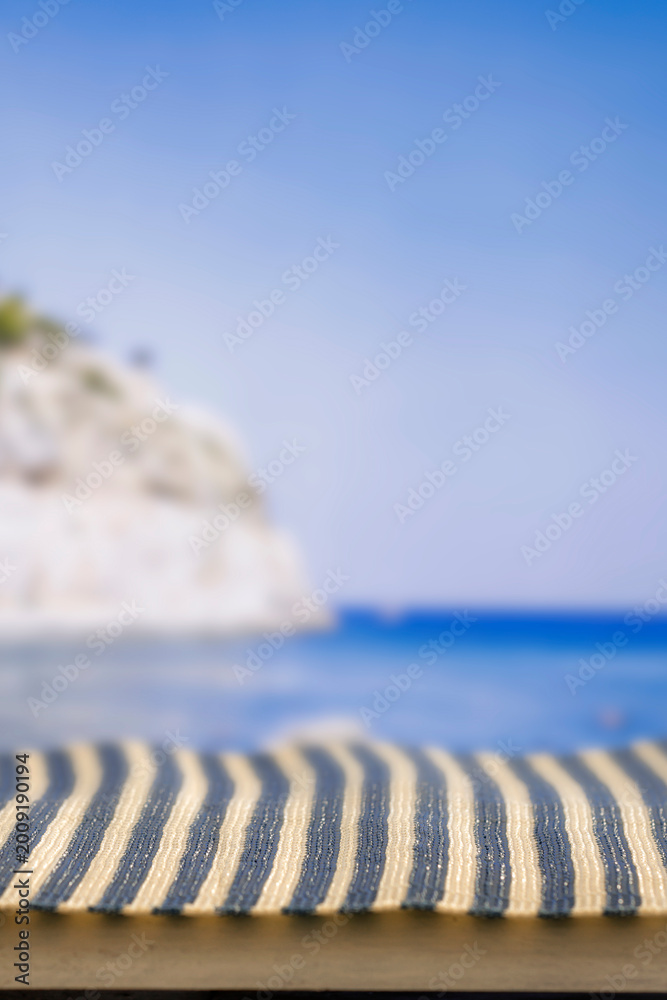 Fototapeta premium Minimal summer composition featuring clean sandy beach with empty copy space for product placement. Rocky coastline meets the sea under bright blue sky, creating natural and scenic atmosphere.