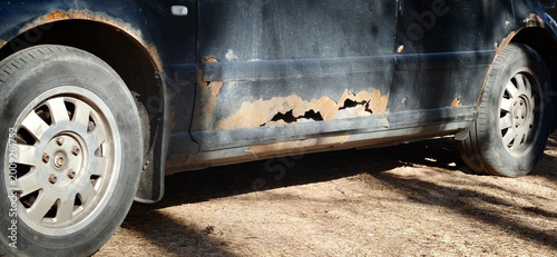 Foto Rusty car with visible corrosion on the side panel parked on a dirt surface, sho