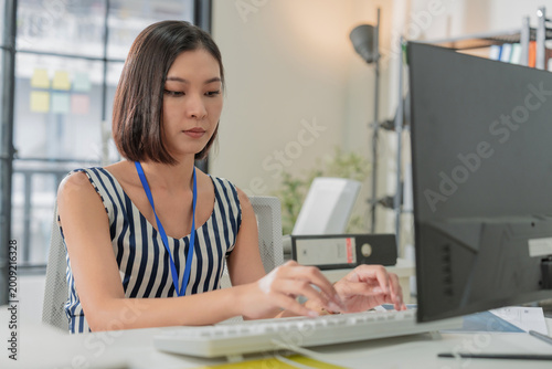 Young Asian businesswoman working on laptop in modern office, concentrated female employee typing on computer at creative workspace