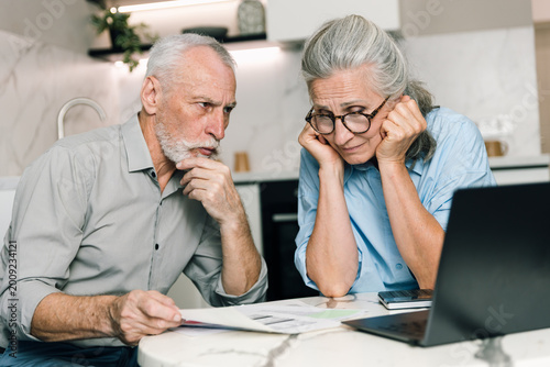 Elderly couple reviews bills and budgets on laptop at home in living space