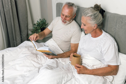 Senior couple happily reading book together in bed