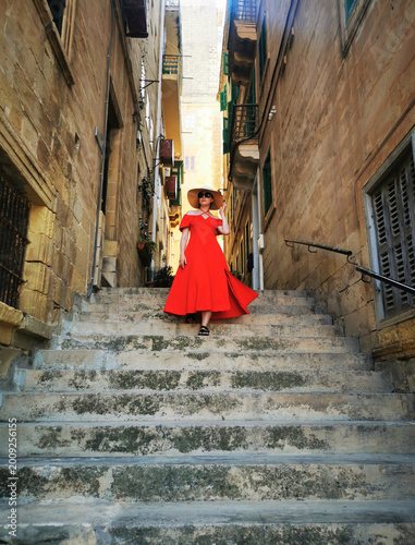 Person descending a narrow stone staircase between historic Maltese buildings. The image conveys the concept of urban exploration and traditional architectural scenery.