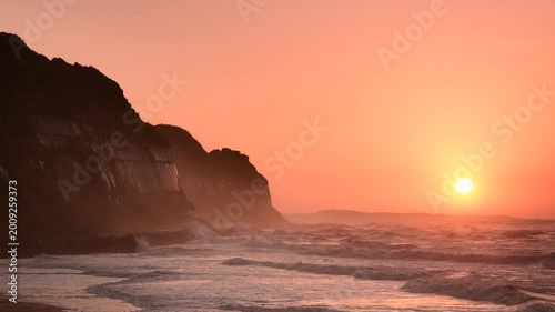 千葉県旭市の屏風ヶ浦、春の早朝に朝焼けと日の出が太平洋の荒波を照らす断崖の海岸風景