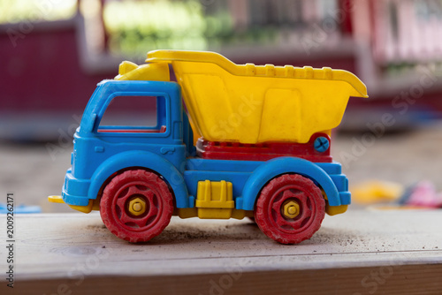 Fotografia A colorful, well-worn plastic toy dump truck sits on a dusty outdoor surface at kindergarten