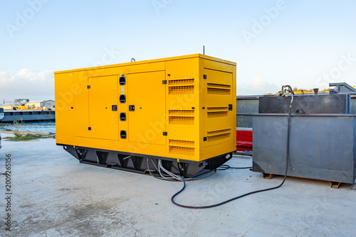 Obraz na płótnie Large industrial diesel generator in yellow soundproof canopy outdoors on a conc