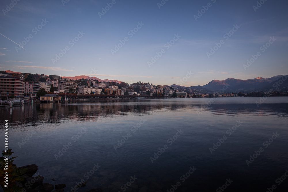 Fototapeta premium Panorama of Lugano luxury houses and hotels in autumn early morning with Swiss and Italian mountains in the background. Lugano, Ticino, Switzerland