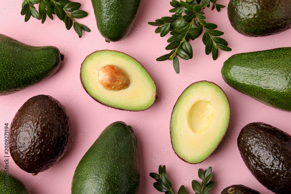 Fototapeta premium Fresh ripe avocados and green leaves on pink background, flat lay