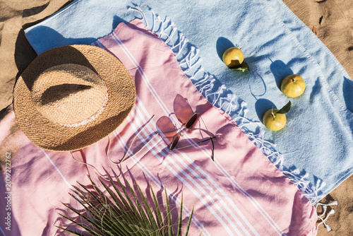 Summer beach accessories flat lay on sand background. Holiday travel, tropical concept. Straw hat, sunglasses, towel and fruits. Sun shadow and sunlight