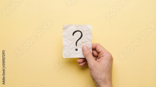 caucasian hand holding crumpled paper with black question mark against yellow background. concept of uncertainty, faq, problem solving. banner, website header, copyspace.