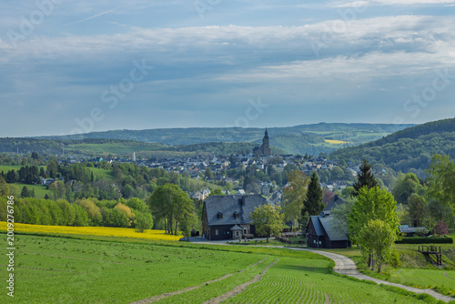 Malerische sächsische Mittelgebirgslandschaft mit blühenden Rapsfeldern und Blick auf die Bergstadt Schneeberg im Erzgebirge