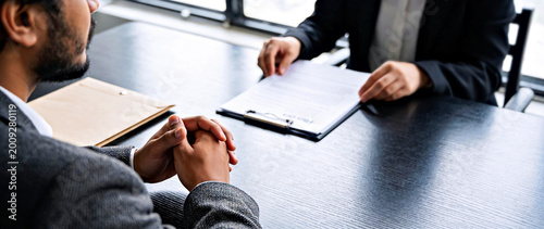 Over the Shoulder View of Applicant Seated at Table with Documents at Job Interview in Modern Office