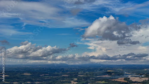 A wide-angle composition that highlights the contrast between a dynamic, cloud-laden sky and the vast, varied vegetation at its base.