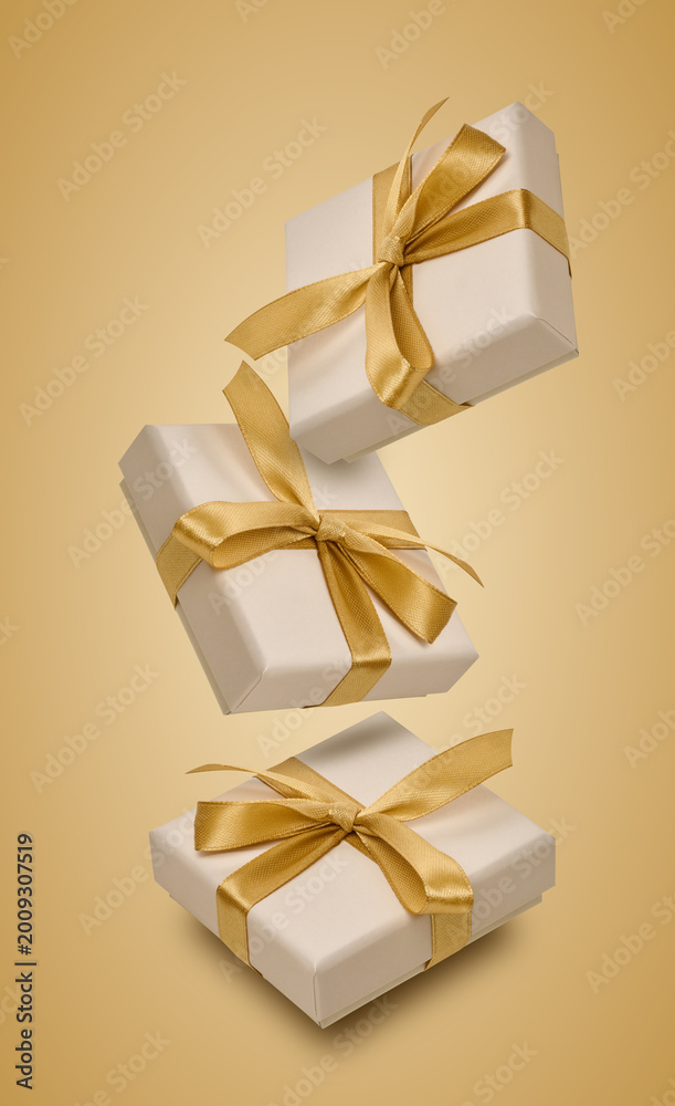Fototapeta premium Floating beige gift boxes with gold satin ribbons and bows.