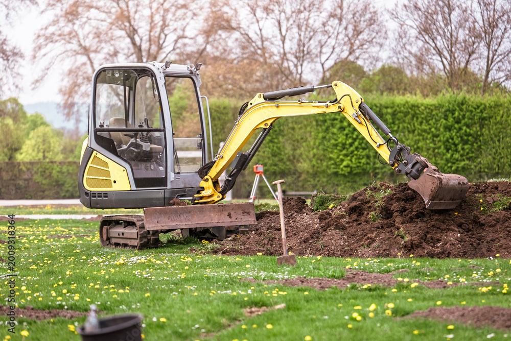 Fototapeta premium Compact excavator working in garden yard landscaping and ground preparation