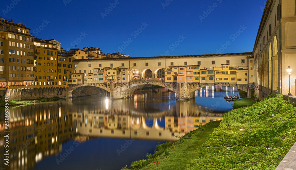 Fototapeta premium Cityscape with the Ponte Vecchio, a medieval stone arch bridge over the Arno, in Florence, Italy. Night view of the bridge. Long exposure. Family vacation in Italy.