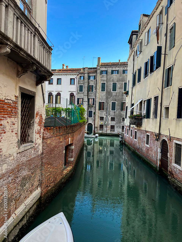 Obraz na plátne Narrow canal in Venice surrounded by historic buildings with reflections in calm water